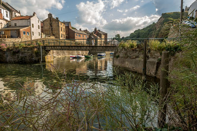 Bridge over river by buildings in city against sky