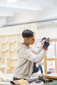 Male teenage trainee rubbing sand paper on wooden table at workbench