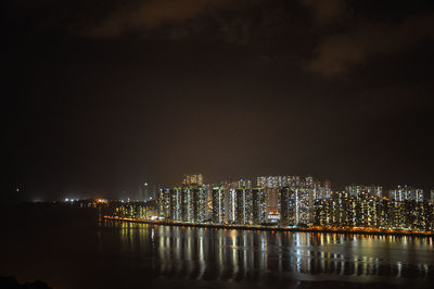 Illuminated buildings by river against sky at night