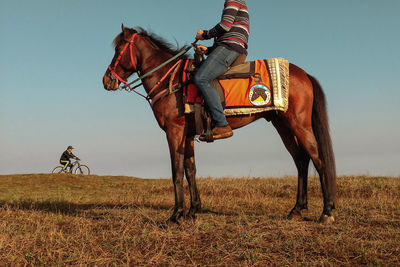 Low section of man riding horse on field against sky