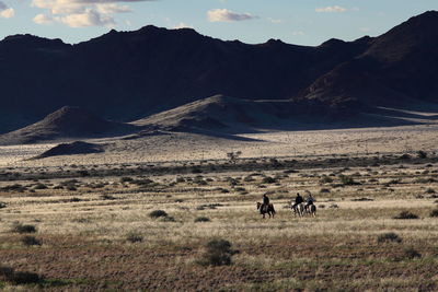 People riding horses on field against mountain