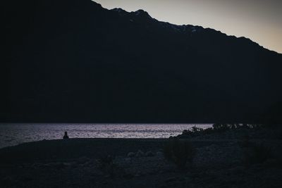 Scenic view of sea by silhouette mountain against sky