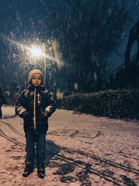 Full length of boys standing on snowy field during snowfall at night