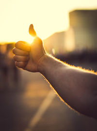 Cropped hand of man gesturing thumbs up during sunset