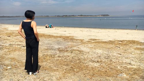 Rear view of woman standing at beach during sunny day