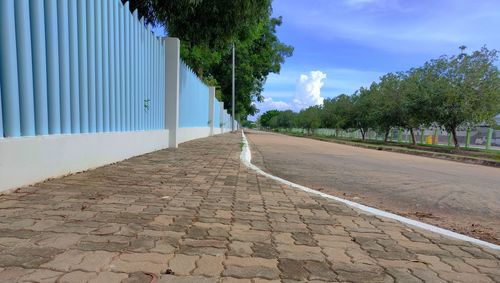 Empty footpath by road against blue sky
