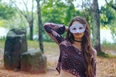Portrait of smiling young woman wearing venetian mask against trees