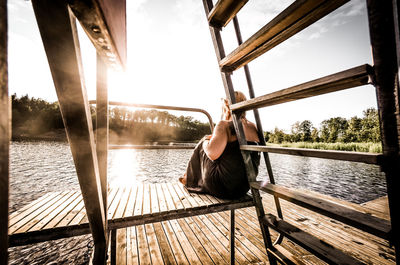 Rear view of woman sitting by lake against sky