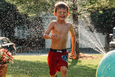 Water splashing on shirtless boy running in yard