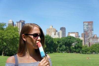 Young woman eating flavored ice in city during sunny day