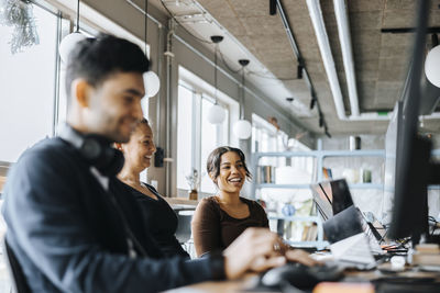 Happy female programmers sitting with male colleague working at office