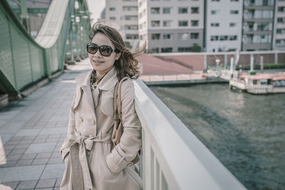 Young woman wearing sunglasses standing against buildings in city