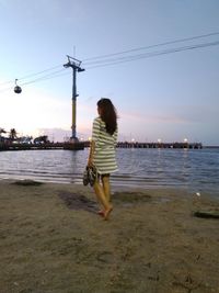 Rear view of woman on beach against sky during sunset