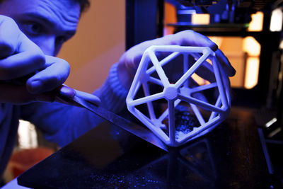 Man using a spatula to separate a 3d geometric figure from the platform of a 3d printer