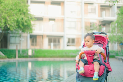 Cute boy sitting on stroller by swimming pool