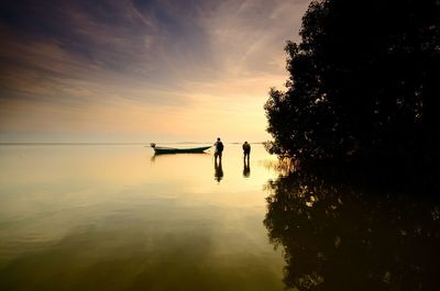 Silhouette people on shore against sky during sunset