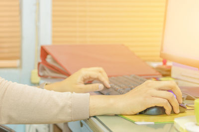 Cropped hands of woman using computer keyboard and mouse at desk