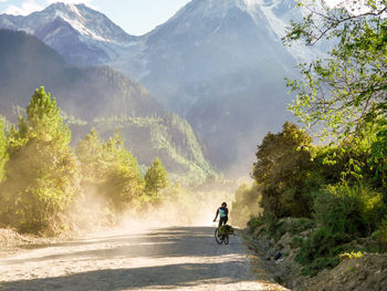 Man riding bicycle on dirt road against mountains