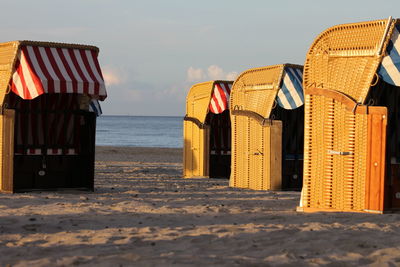 Hooded chairs at beach against sky