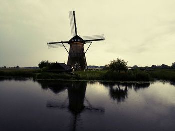 Traditional windmill by lake against sky