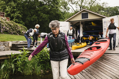 Senior woman and man carrying kayak on jetty during kayaking course