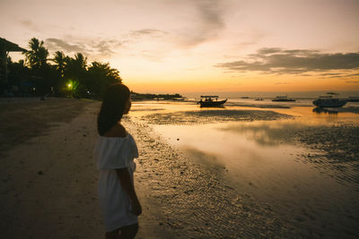 Woman standing on beach against sky during sunset