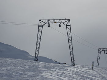 Ski lift over snow covered mountains against sky