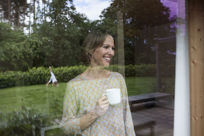 Smiling woman holding cup looking out of window