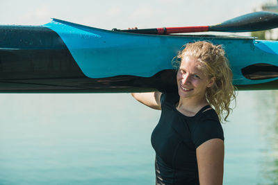 Portrait of smiling young woman carrying kayak