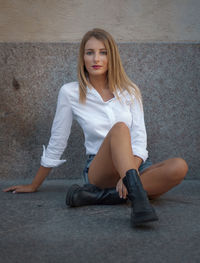 Portrait of young woman sitting against wall