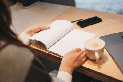 Cropped image of hand holding coffee cup on table