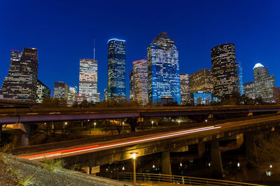 Illuminated bridge and buildings against clear blue sky at night