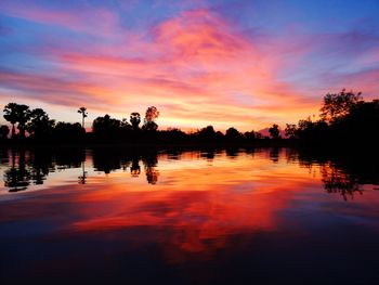 Silhouette trees by lake against romantic sky at sunset