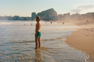 Rear view of man standing at copacabana beach on the sunset 