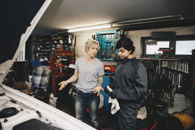 Customer gesturing while talking with female mechanic at auto repair shop