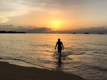 Silhouette woman walking at beach against sky during sunset