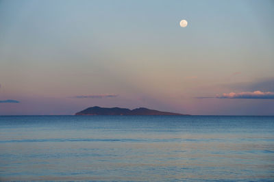 Scenic view of sea against sky and island during sunset with moon