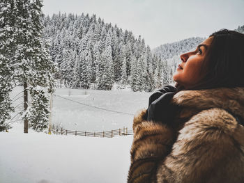 Woman looking up while standing on snow covered land