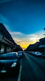 Traffic on road against buildings at sunset