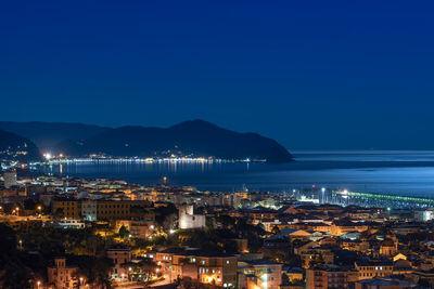 Illuminated city by sea against clear blue sky