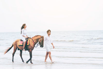 Women riding horses on beach against sky