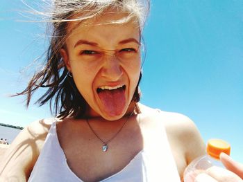 Low angle view of young woman sticking out tongue against sky