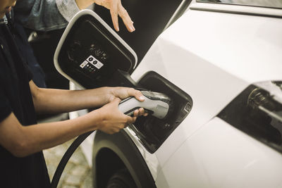 Hands of boy plugging in cable while charging electric car