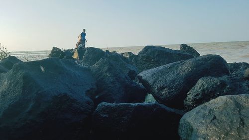 Man standing on rock in sea against clear sky