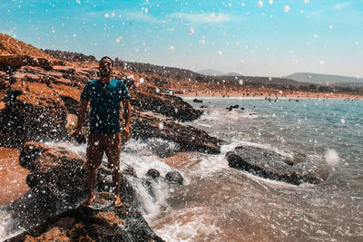 Man standing at beach with splashing water against sky
