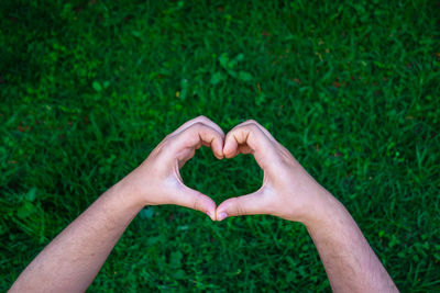 Cropped hands of man making heart shape over grassy field