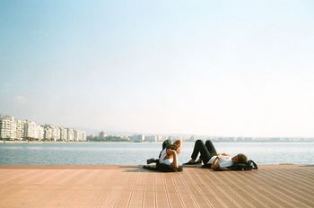 FRIENDS SITTING ON SHORE AGAINST SKY