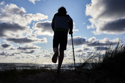 Rear view of man standing on beach against sky