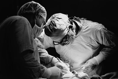 Surgeons operating patient against black background