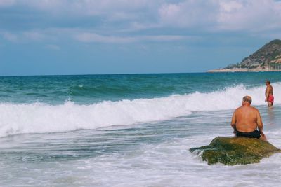 Rear view of shirtless man in sea against sky